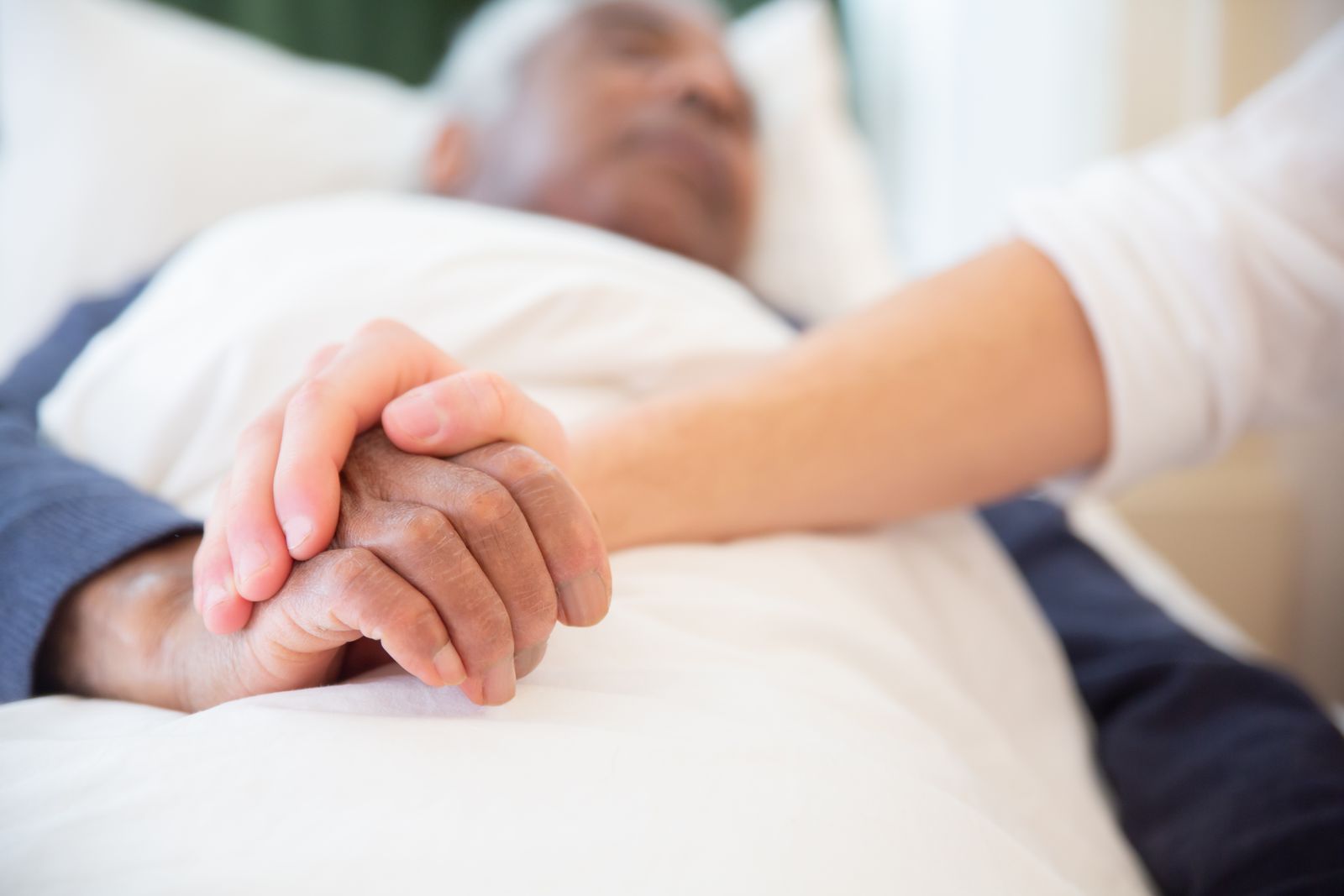 Hands held at a hospital bedside, the care end of life care expert witnesses give evidence about